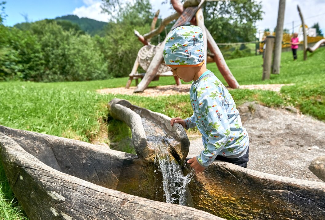 Junge spielt mit Wasser an einem Holzbrunnen auf einem Spielplatz