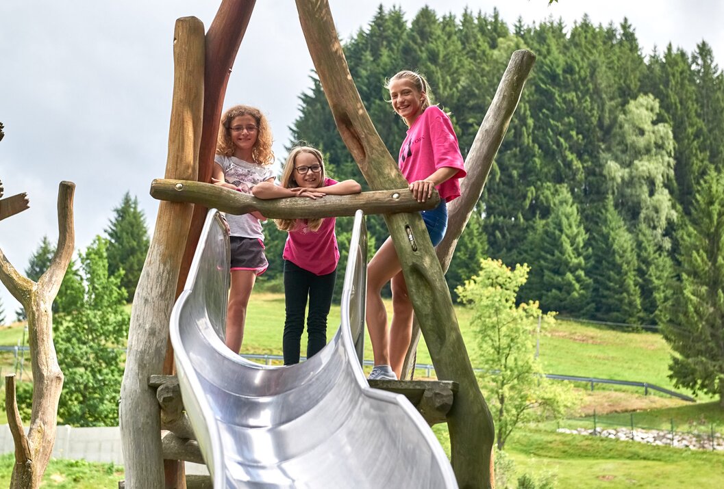 Drei Mädchen stehen auf einem Spielplatz an einer Rutsche
