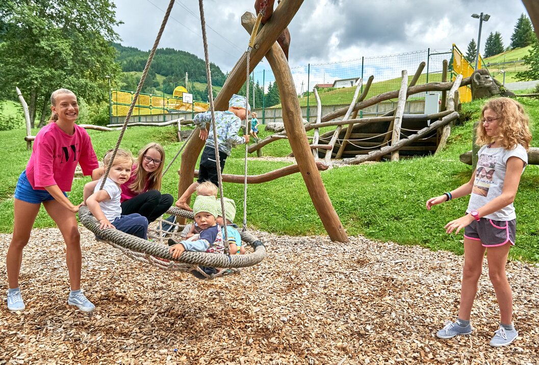Kinder spielen auf einem Spielplatz mit Schaukel, Klettergerüst und Holzboden