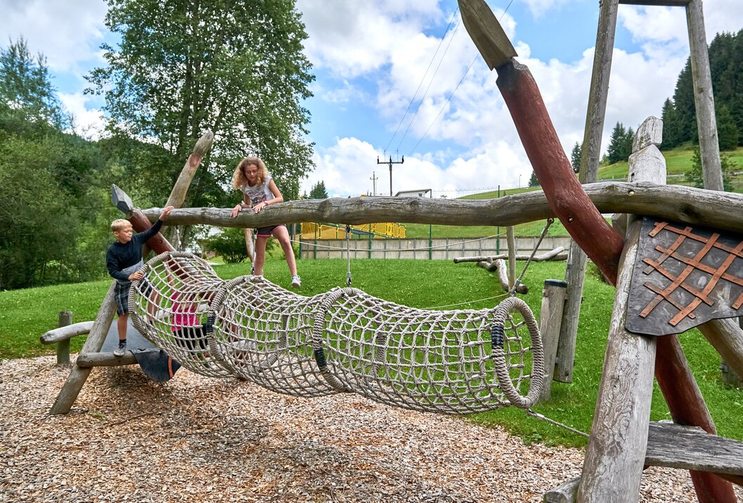 Kinder spielen auf einem Spielplatz mit Netzbrücke und Holzelementen