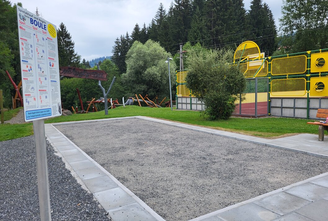 Boulodrome mit Kiesfläche, umgeben von Grünfläche und Bäumen