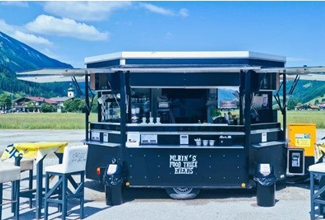 Schwarzer Foodtruck mit Aufschrift vor Bergkulisse und blauem Himmel