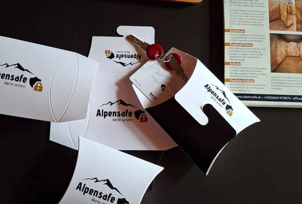 Alpensafe-Verpackungen, Schlüssel, Stift und Broschüre auf dunkler Oberfläche