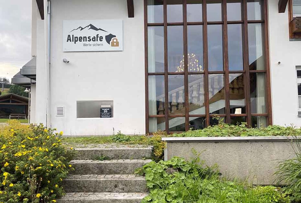 Weißes Gebäude mit großem Fenster, Treppe und AlpenSafe-Schild