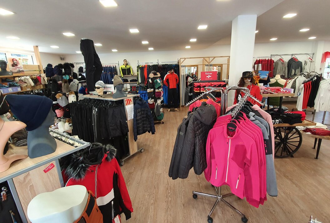 Innenansicht eines Bekleidungsgeschäfts mit Kleiderständern und Regalen voller Jacken und anderer Kleidungsstücke
