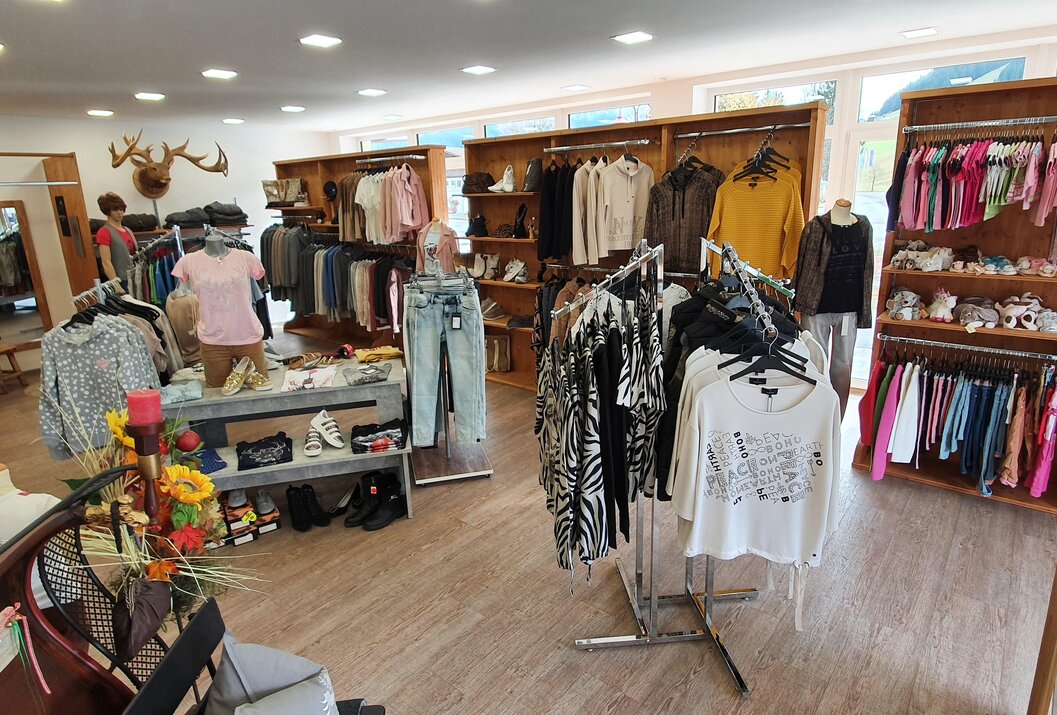 Innenansicht eines Bekleidungsgeschäfts mit Kleidung auf Kleiderbügeln und Regalen
