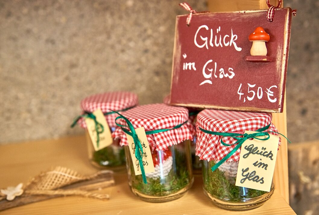 Gläser mit Moos und Miniatur-Fliegenpilzen, bedeckt mit rot-weiß karierten Stoffen, Schild Glück im Glas