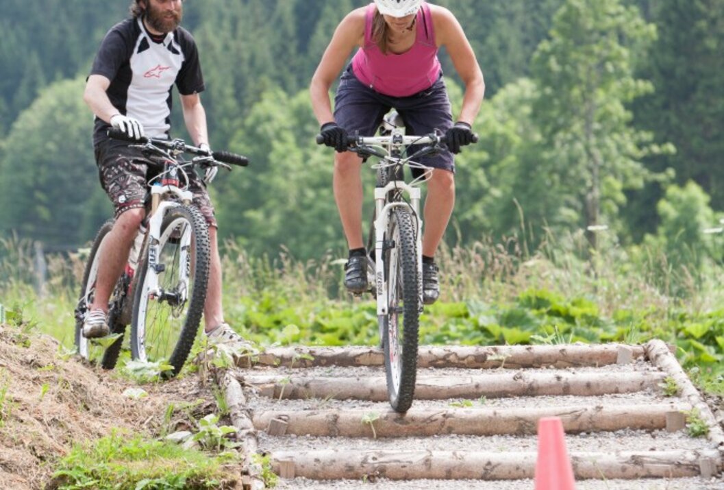 Two mountain bikers with helmets ride over a wooden staircase in the countryside
