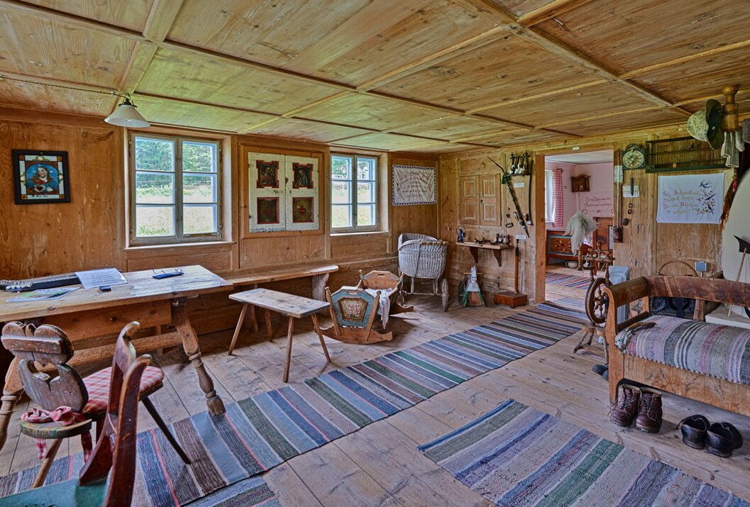 Holzvertäfelter Raum mit alten Möbeln, Teppichstreifen und Blick in einen Nebenraum