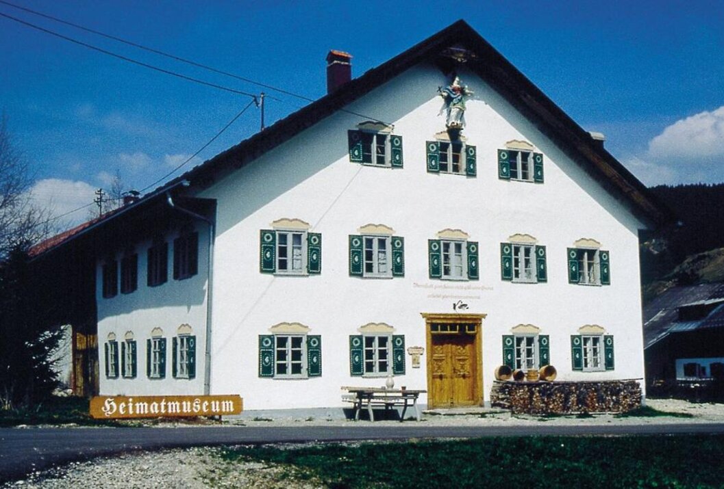 Weißes Haus mit grünen Fensterläden und Holzschild "Heimatmuseum"