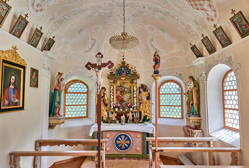 Innenansicht einer kleinen Kapelle mit Altar, Kruzifix, Heiligenfiguren und verzierten Fenstern