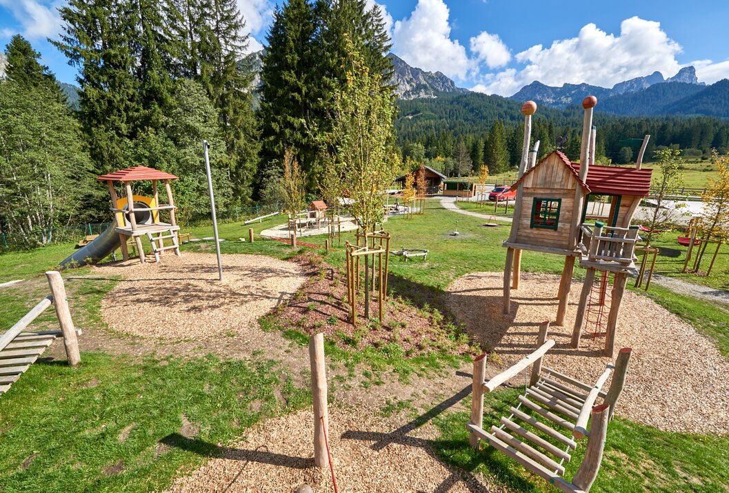 Spielplatz mit Holzturm, Rutsche und Klettergerüst vor Bergkulisse im Grünen