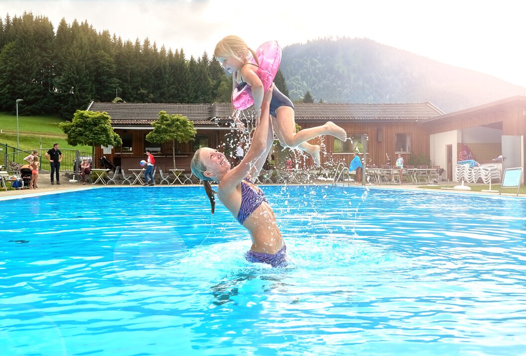 Mutter hebt Mädchen mit Flügeln im Schwimmbad hoch