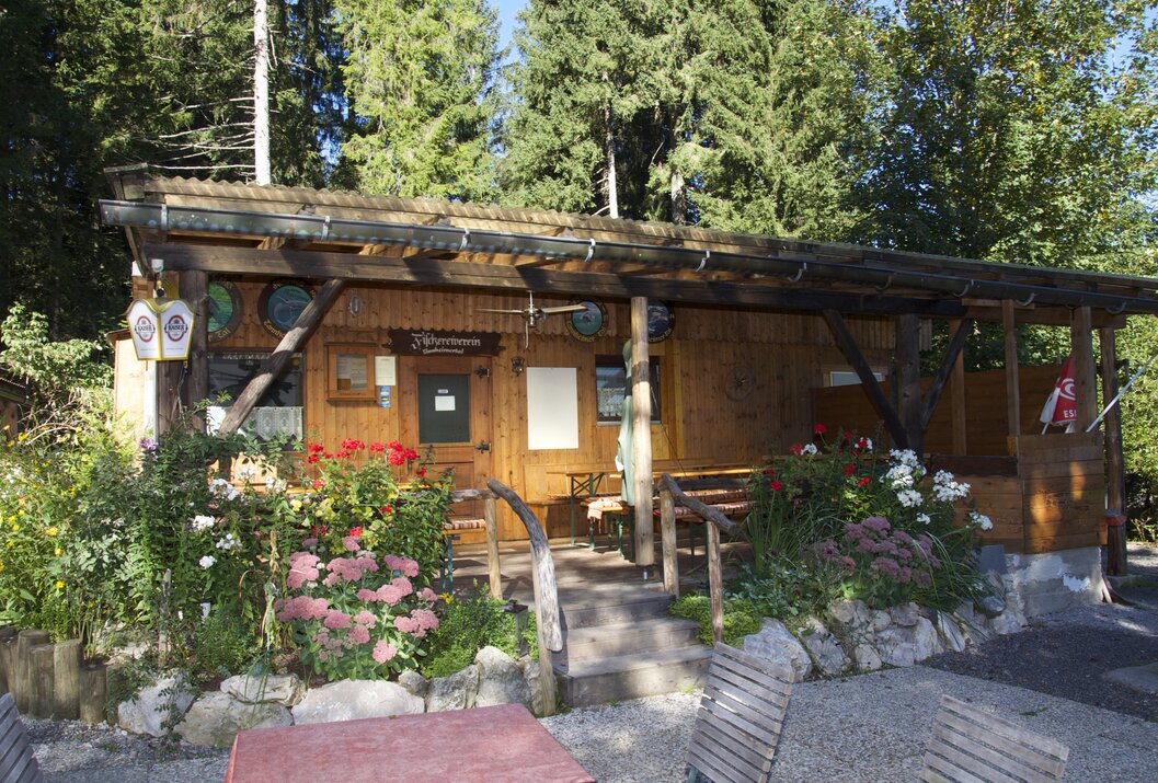Hölzernes Gebäude mit Veranda, umgeben von Blumen und Bäumen