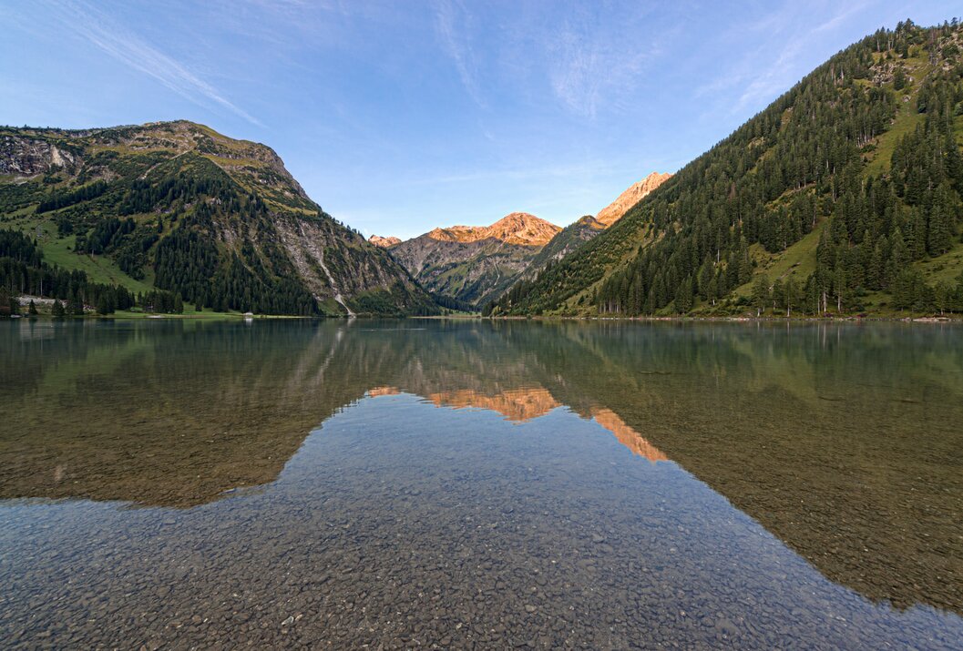 Bergsee mit Spiegelung der Berge im klaren Wasser unter blauem Himmel