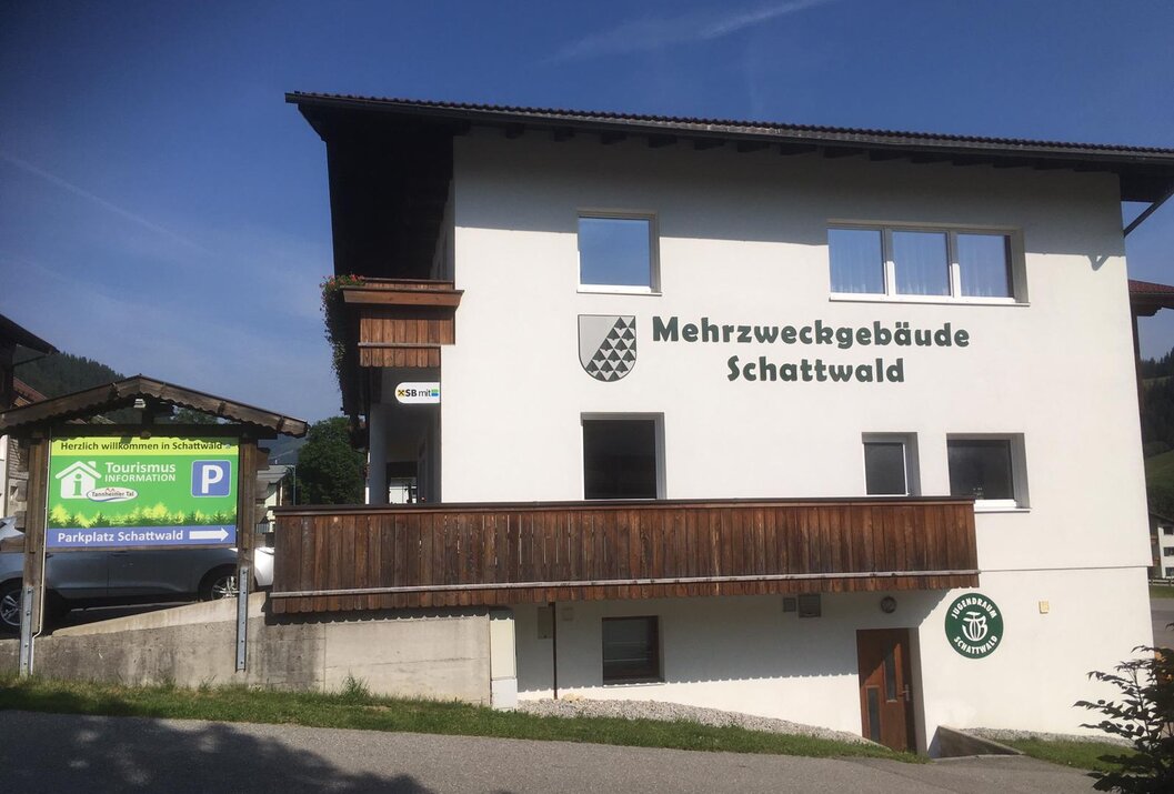 Mehrzweckgebäude Schattwald mit Wappen an weißer Fassade unter blauem Himmel