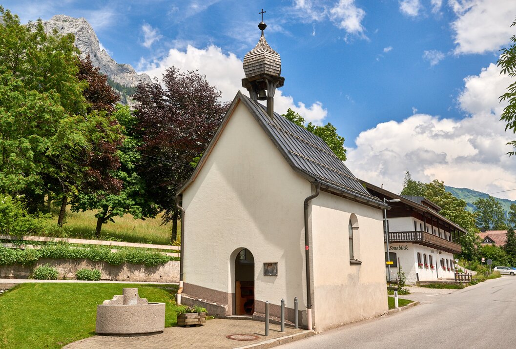 Kleine weiße Kapelle mit Glockenturm vor Bergkulisse und blauem Himmel
