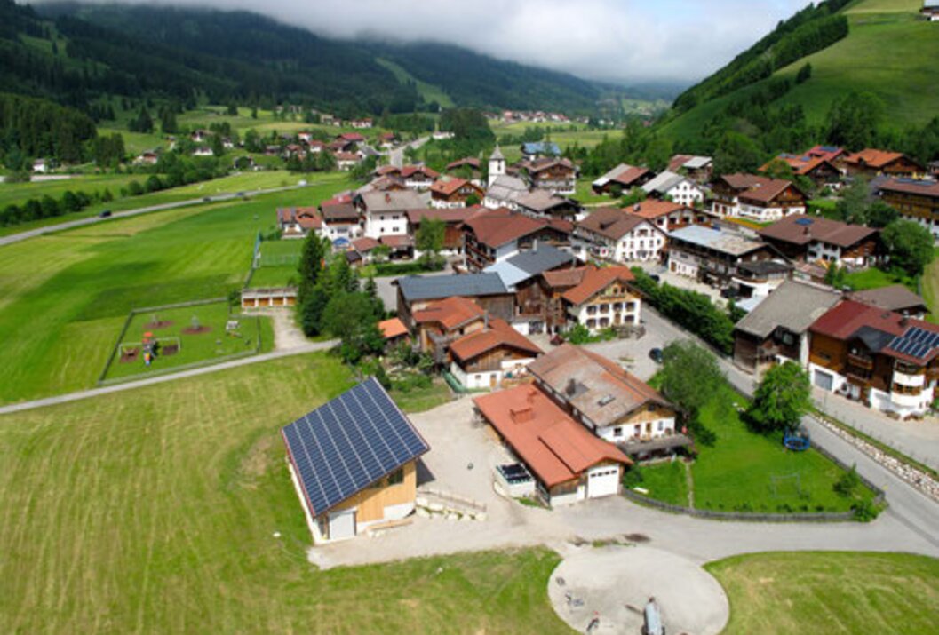 Dorf in grüner Landschaft mit Häusern, Kirche und Bergen im Hintergrund