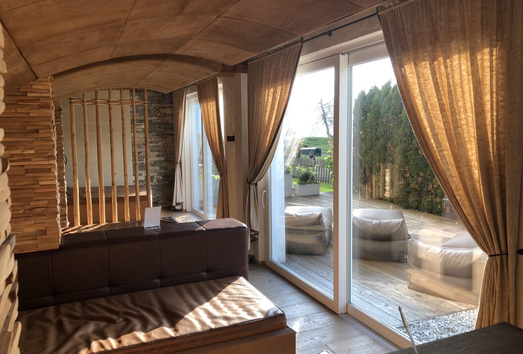 Innenraum mit Couch und Blick durch Glastüren auf Terrasse mit Sitzgelegenheiten