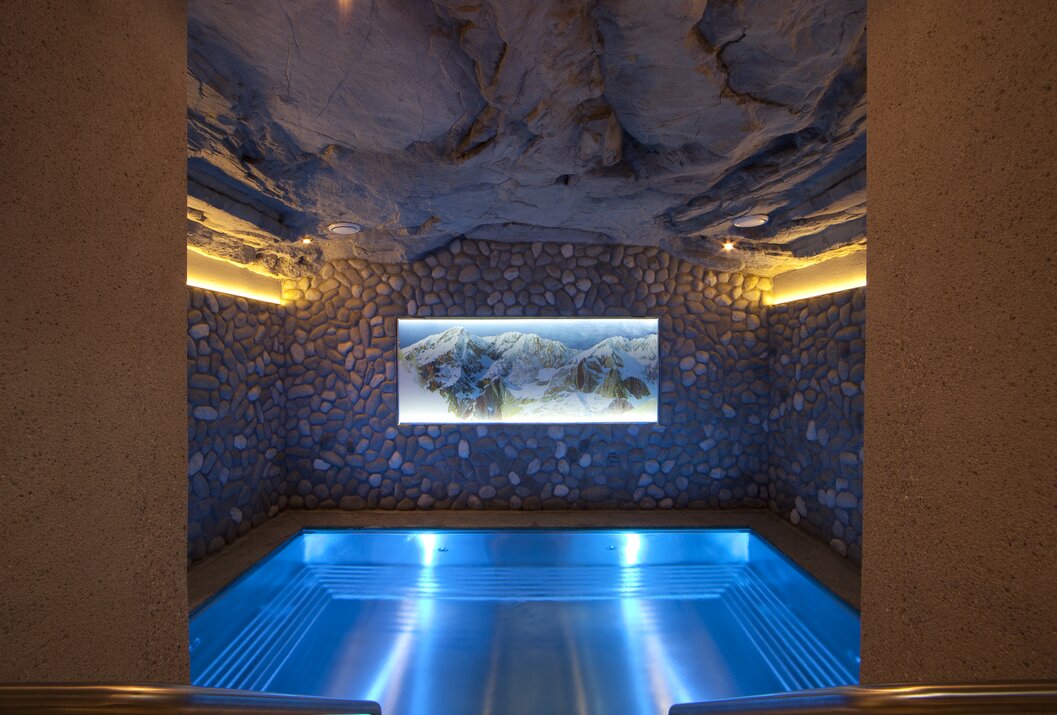 Blauer Pool in einem Raum mit Steinwänden und einer beleuchteten Bergkarte