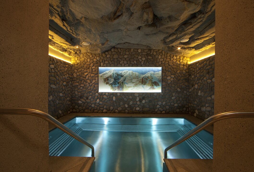 Innenpool mit Steinwand und beleuchtetem Landschaftsbild unter gewölbter Decke