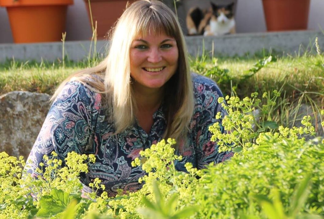 Frau lächelt im Garten, Katze in Blumentopf im Hintergrund