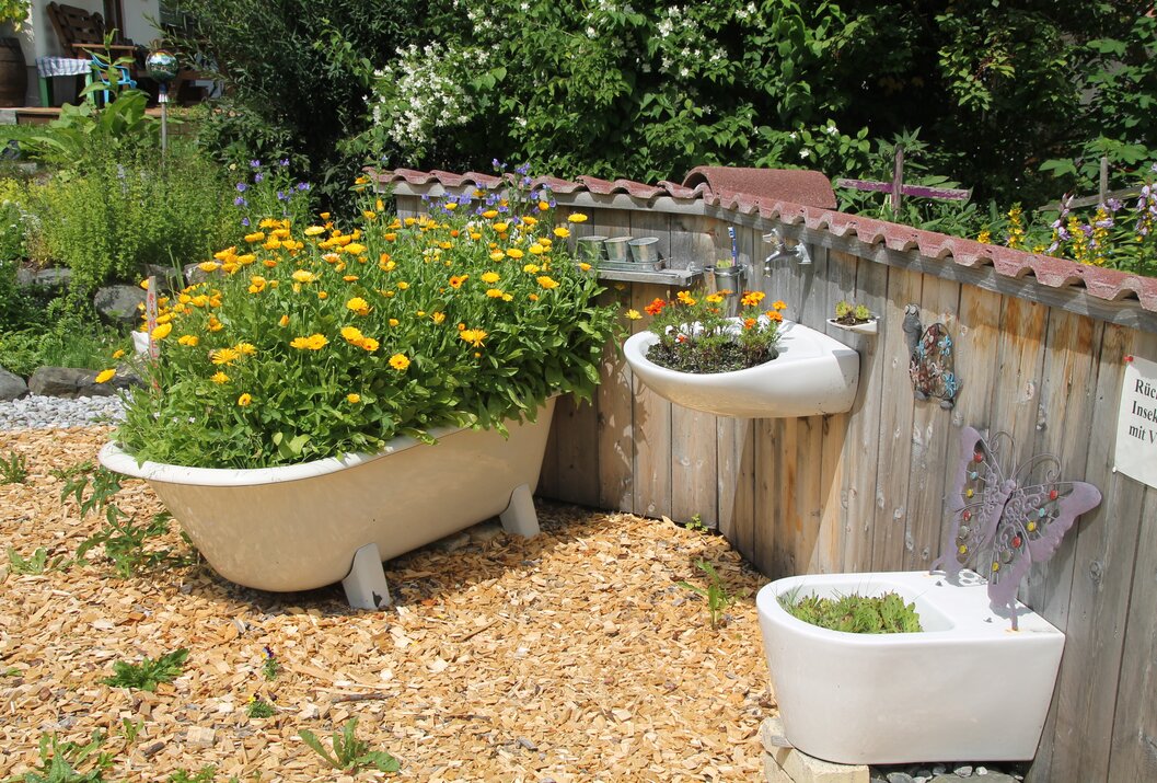 Garten mit Badewanne, Waschbecken und Toilette als ungewöhnliche Pflanzgefäße
