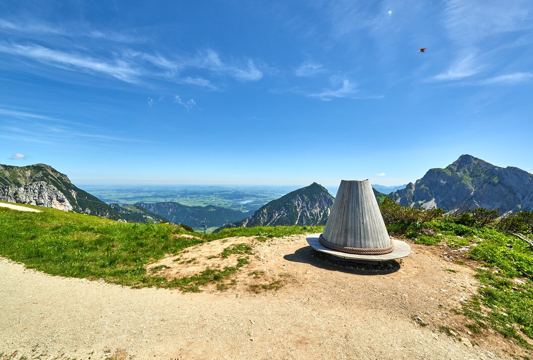 Gipfelkreuz-ähnliche Holzkonstruktion vor Bergpanorama unter blauem Himmel