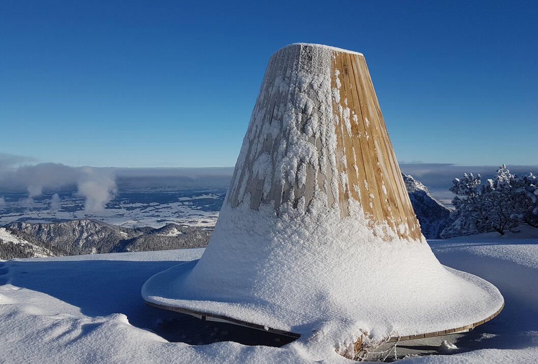 Schneebedecktes Holzgebäude auf Berg mit Blick auf gefrorenes Gewässer unter blauem Himmel