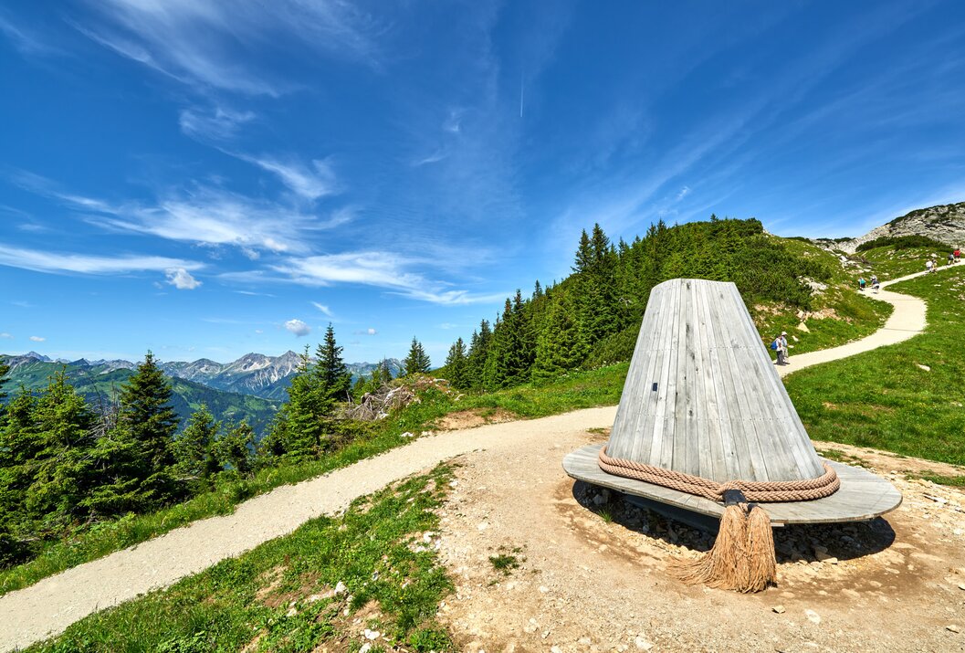 Holzkonstruktion am Wanderweg mit Blick auf grüne Berge und blauen Himmel