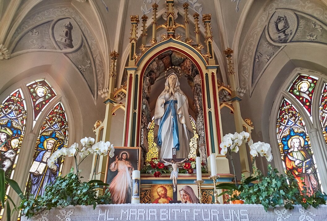 Altar mit Marienstatue, Blumen, Kerzen und Heiligenbildern in einer Kirche