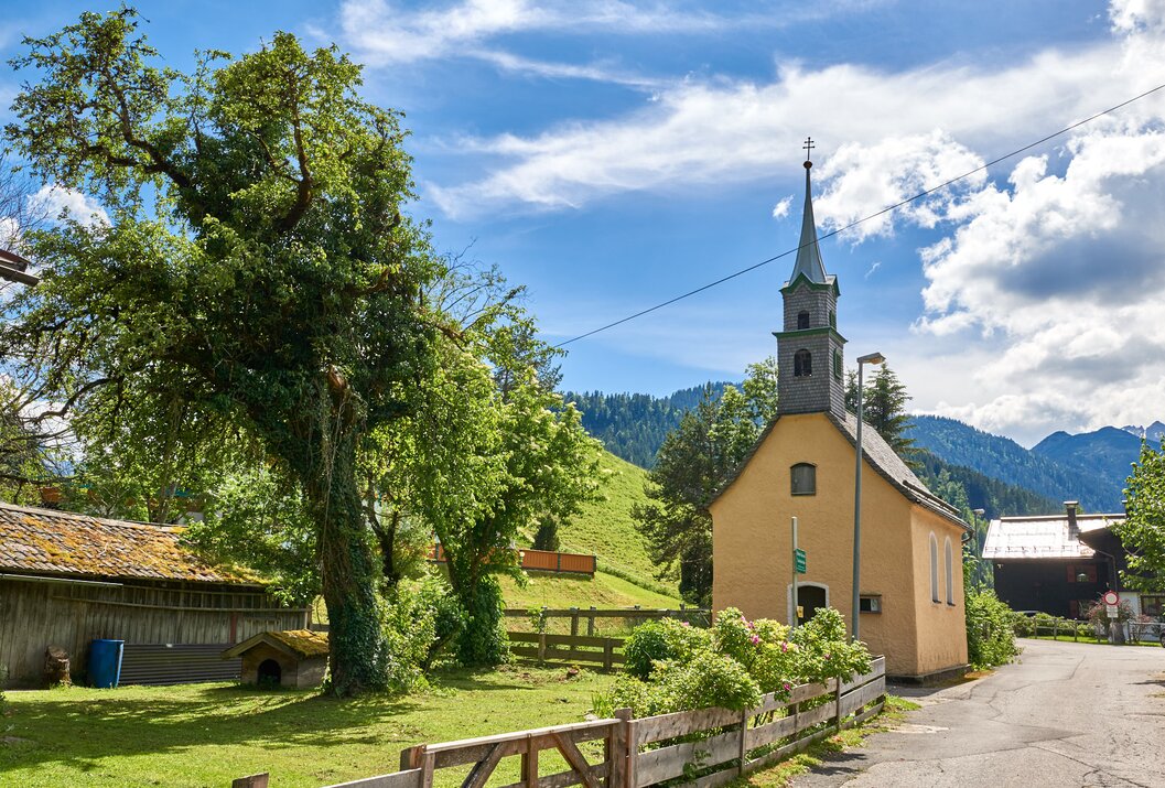 Gelbe Kirche mit Kirchturm vor grüner Hügellandschaft unter blauem Himmel
