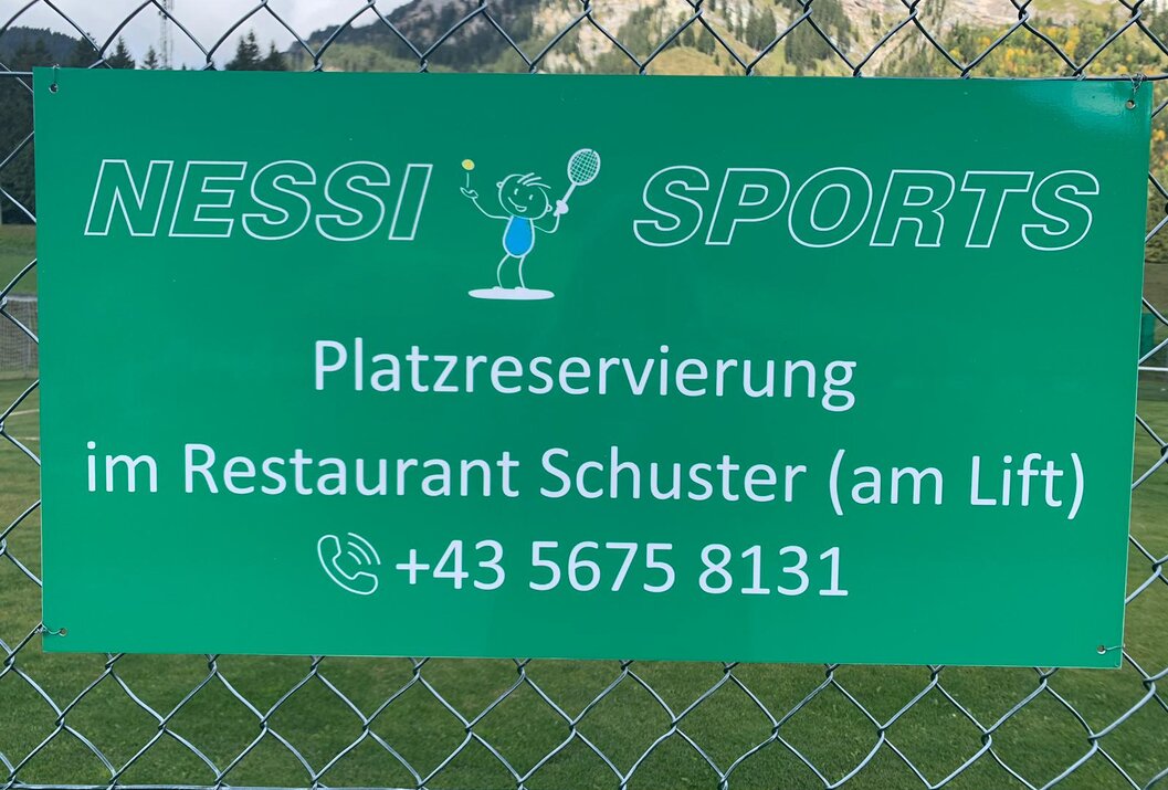 Grünes Schild mit Tennisplatz-Reservierung und Kontaktinformationen vor Bergkulisse