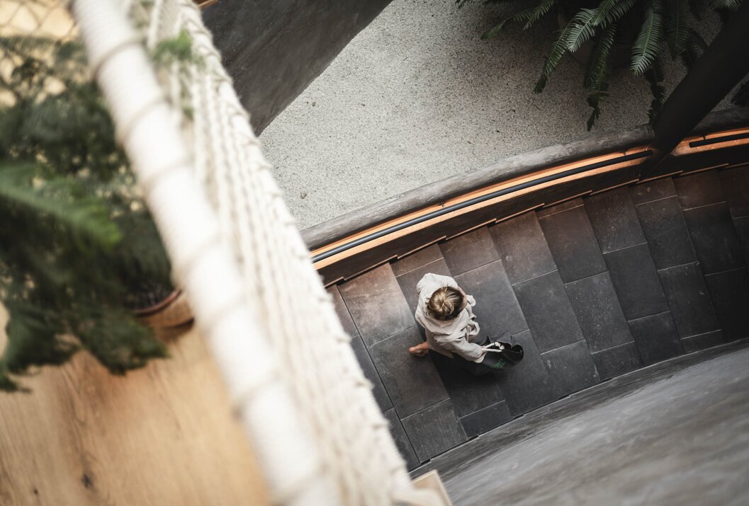 Draufsicht: Person mit Tasche geht Treppe hinunter, Geländer links, Pflanzen rechts