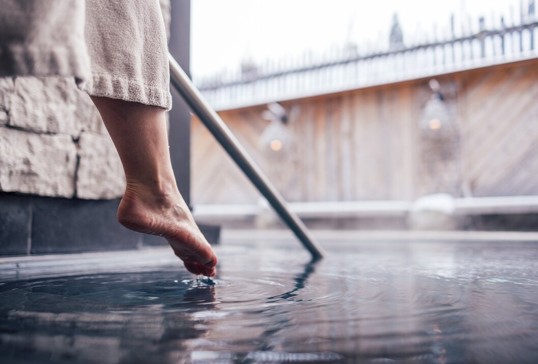Fuß berührt Wasser in einem Pool mit Handlauf und verschwommenem Hintergrund