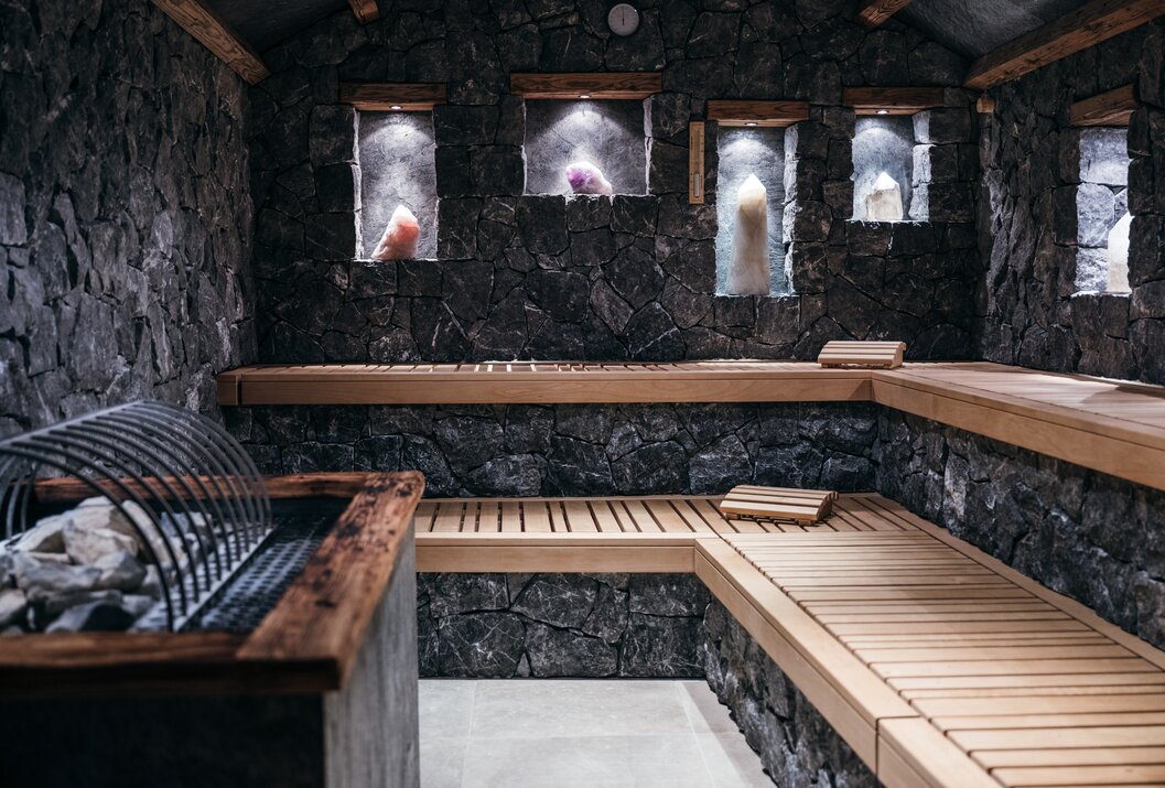 Sauna mit Steinwänden, Holzbänken und beleuchteten Nischen