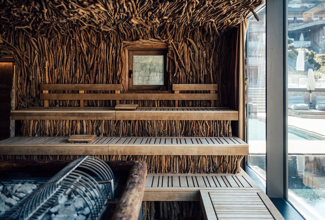 Holzsauna mit Bänken, Ofen und Fenster, Wände und Decke mit Ästen verkleidet
