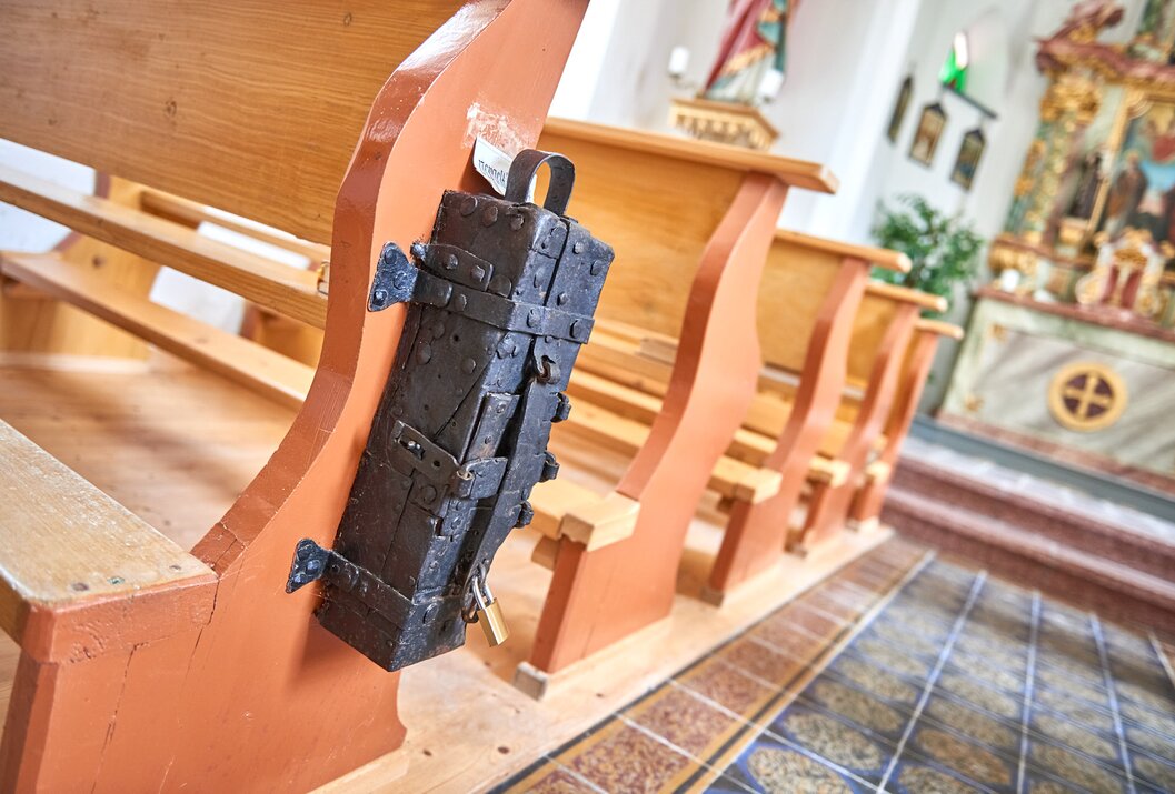 Black, decorated chest hangs on church pew