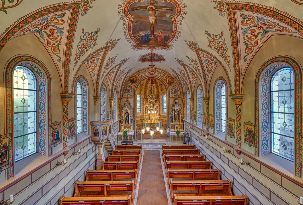 Innenansicht einer Kirche mit verzierten Wänden, Deckenmalerei und Holzbänken