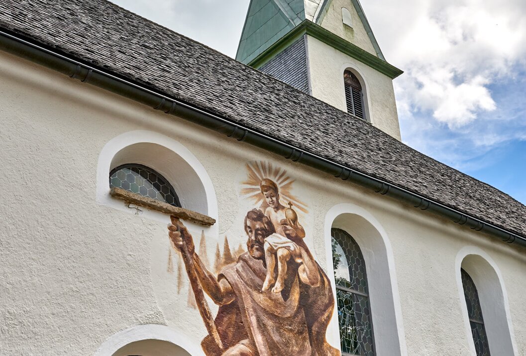 Kirche mit Wandmalerei von Mann mit Kind und Kirchturm unter bewölktem Himmel