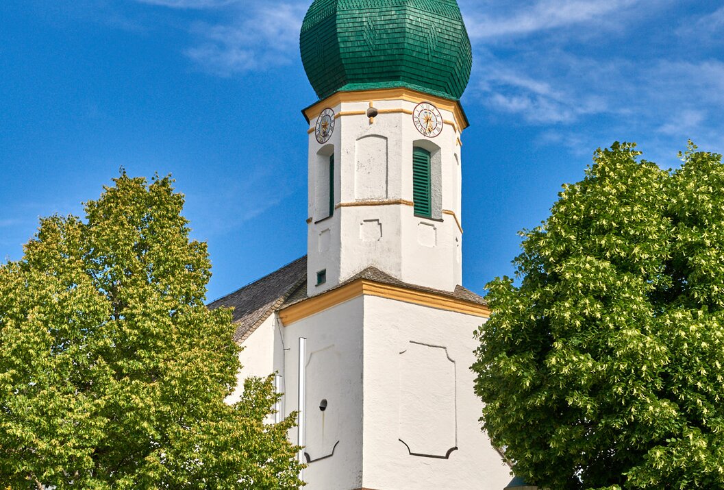 Church tower with green dome against blue sky and trees