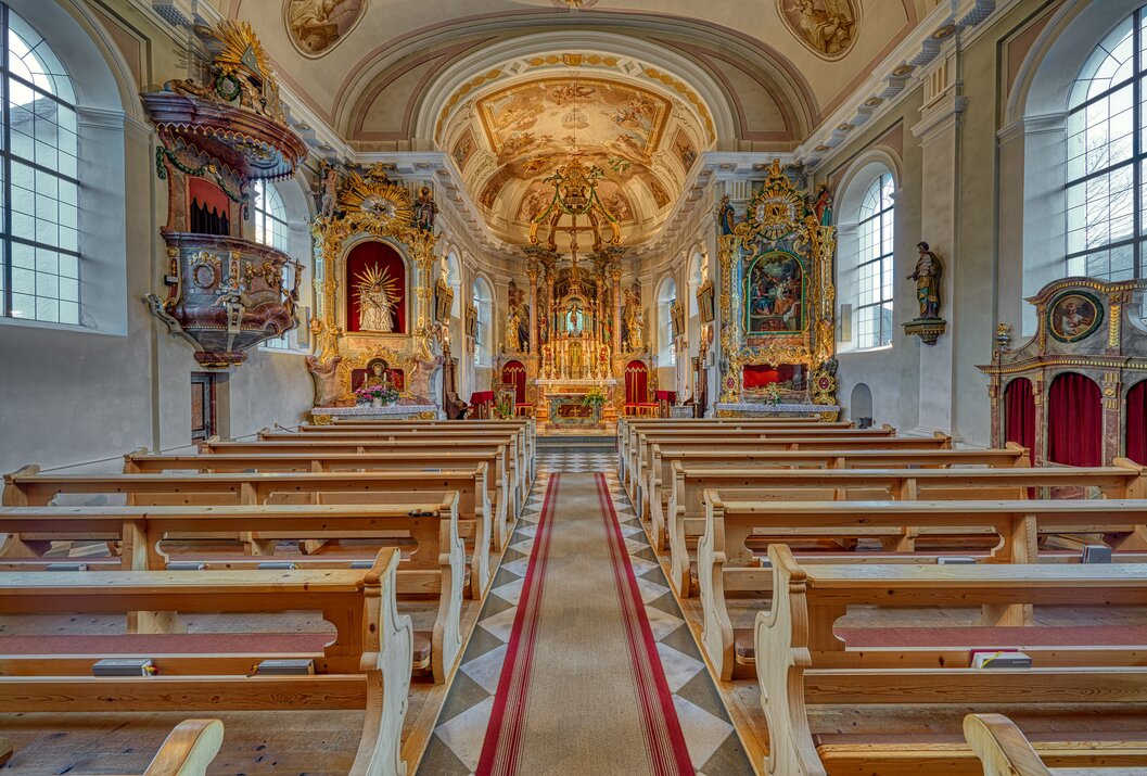 Interior view of a richly decorated church with benches and altar