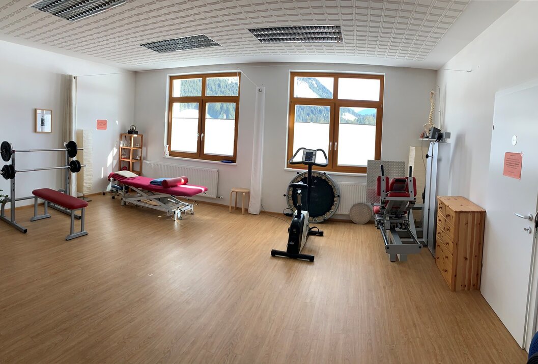 Heller Raum mit Therapiebank, Trainingsgeräten und zwei Fenstern