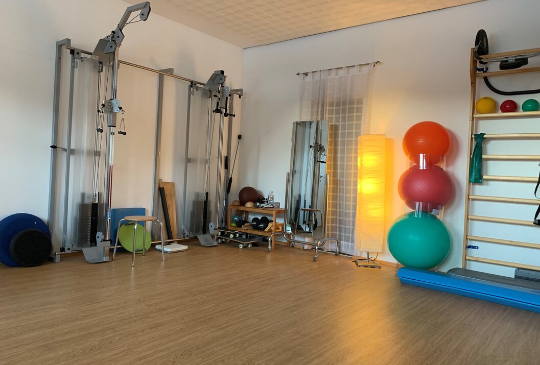 Heller Therapieraum mit Trainingsgeräten, Spiegel, Gymnastikbällen und Sprossenwand