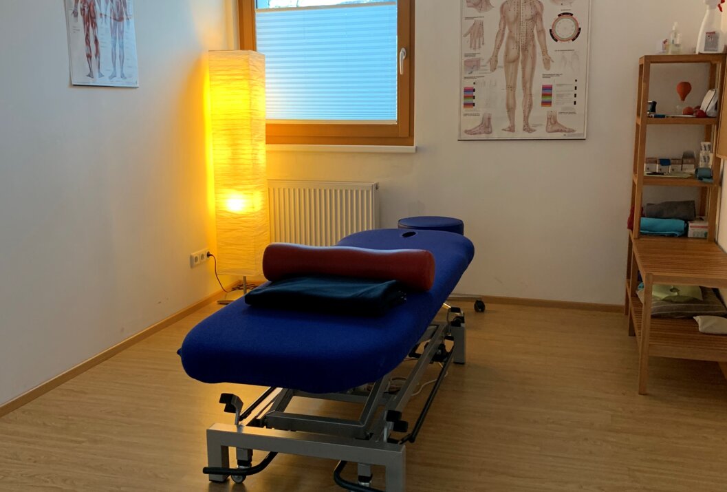 Behandlungsliege in Praxis mit Anatomiepostern und Fenster