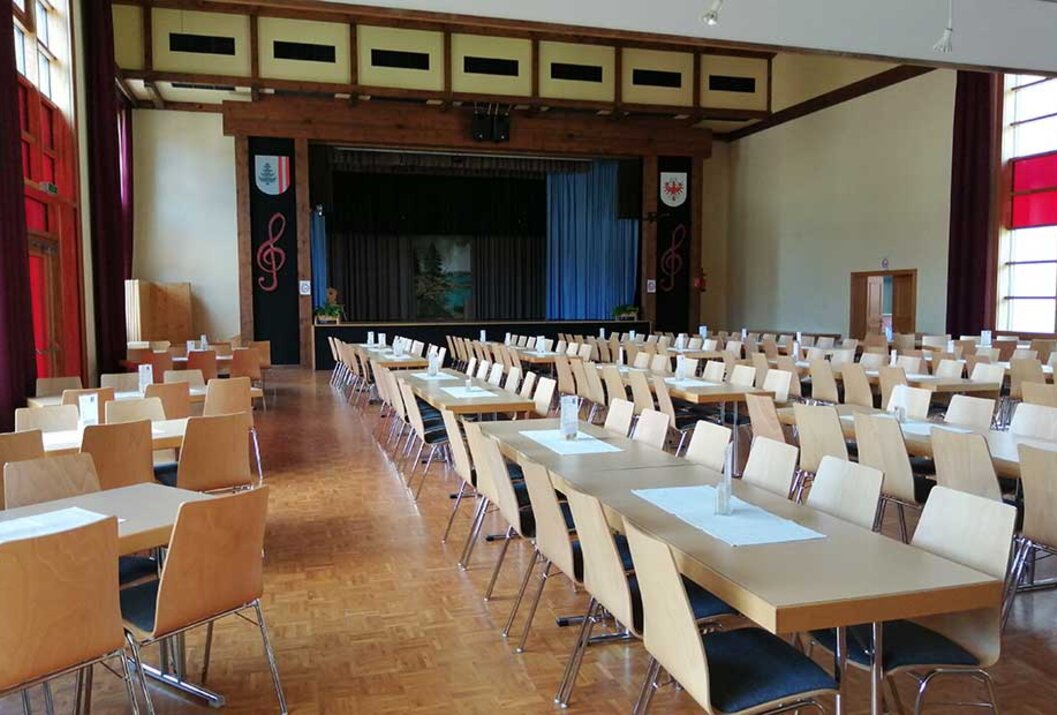 Leerer Saal mit Tischen und Stühlen vor einer Bühne mit blauem Vorhang