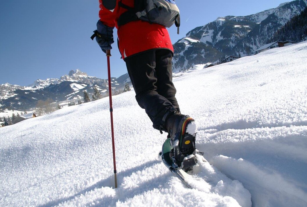 Person mit Schneeschuhen und Wanderstock im Schnee vor Bergkulisse