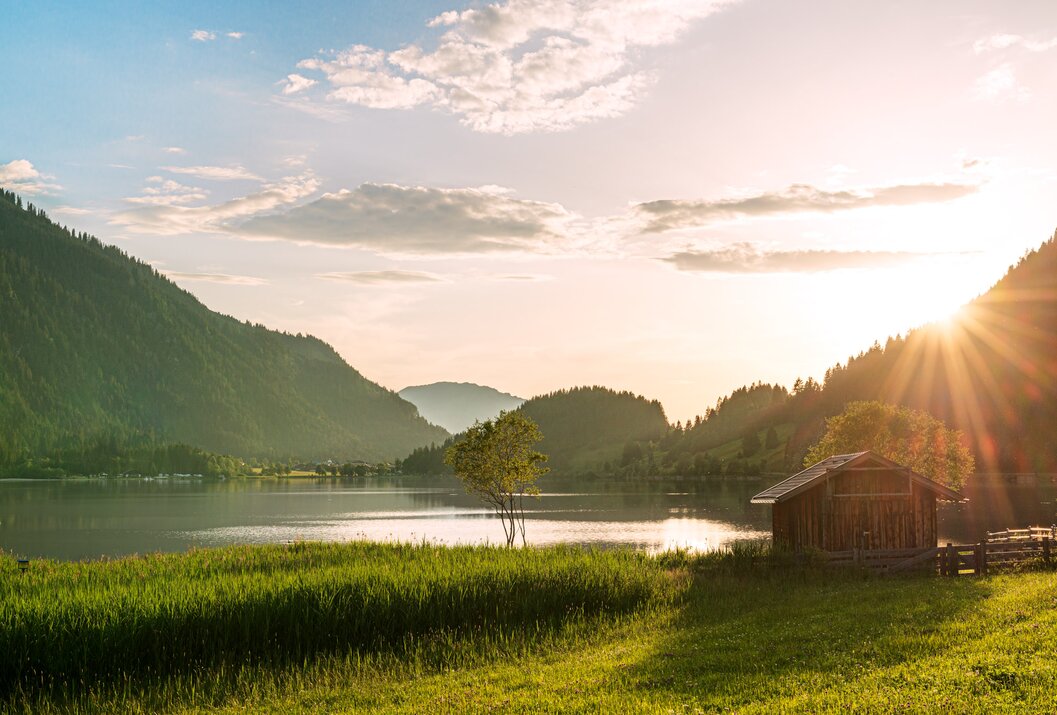 Idyllische Landschaft mit See, Bergen, Wiese und Hütte im Abendlicht