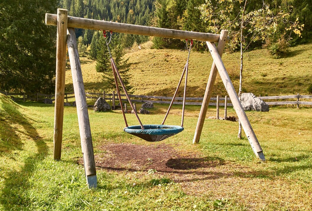 Korbschaukel auf einer Wiese vor hügeliger Landschaft