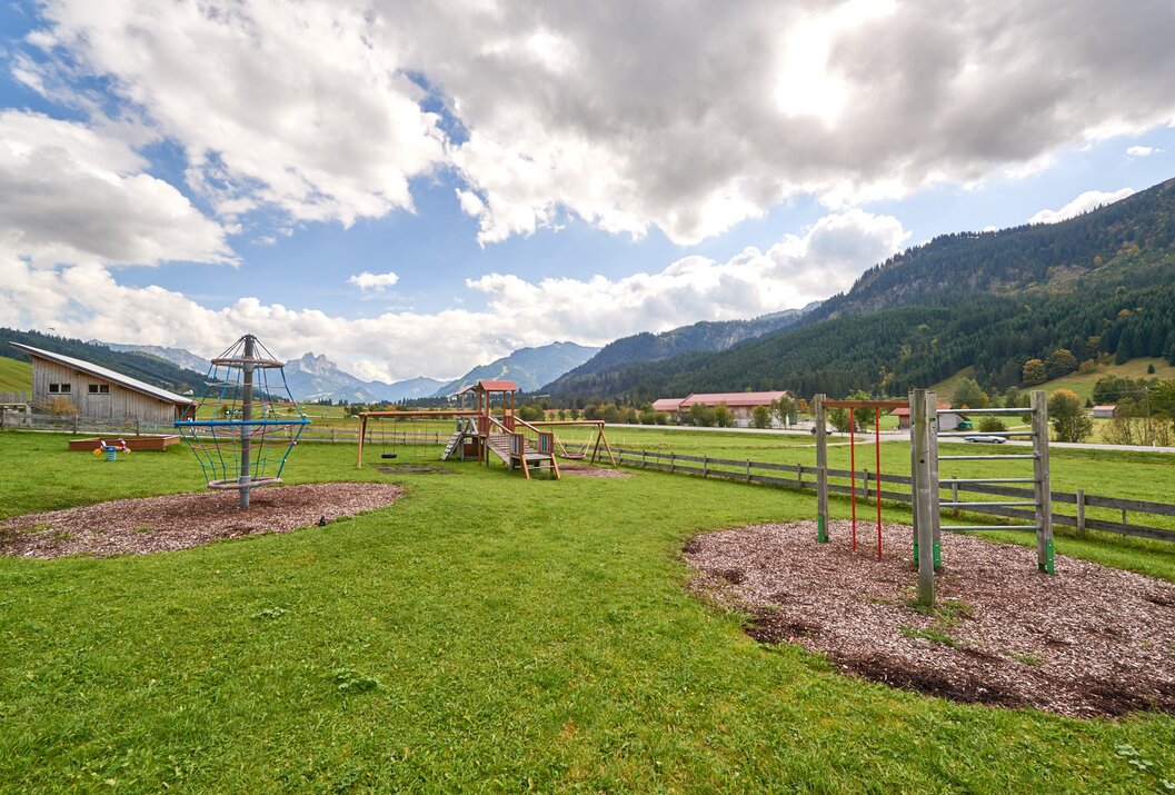 Spielplatz mit Klettergerüst vor Bergkulisse unter bewölktem Himmel